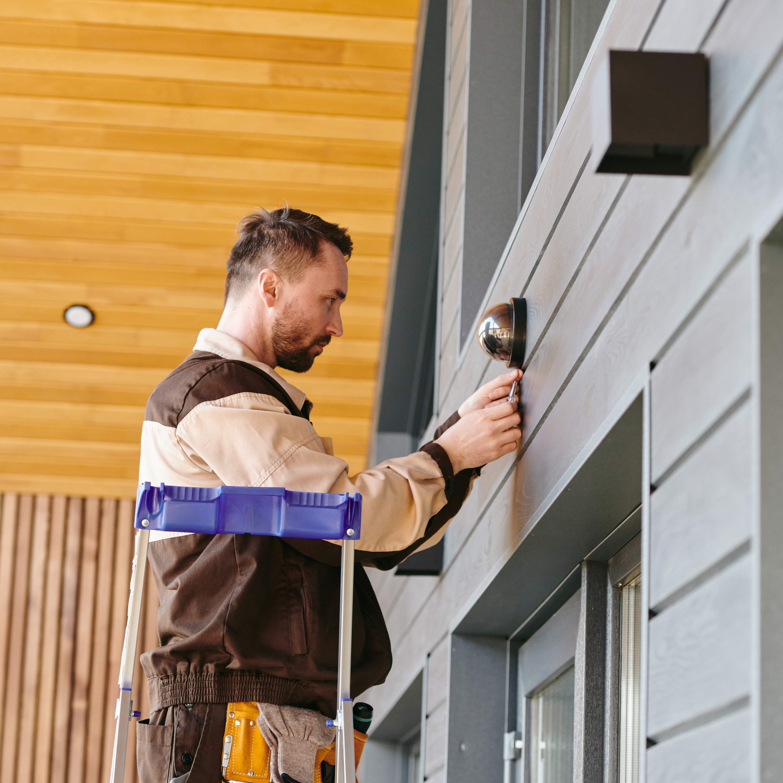 young-man-fixing-alarm-system-on-wall-above-the-do-2023-11-27-05-01-15-utc